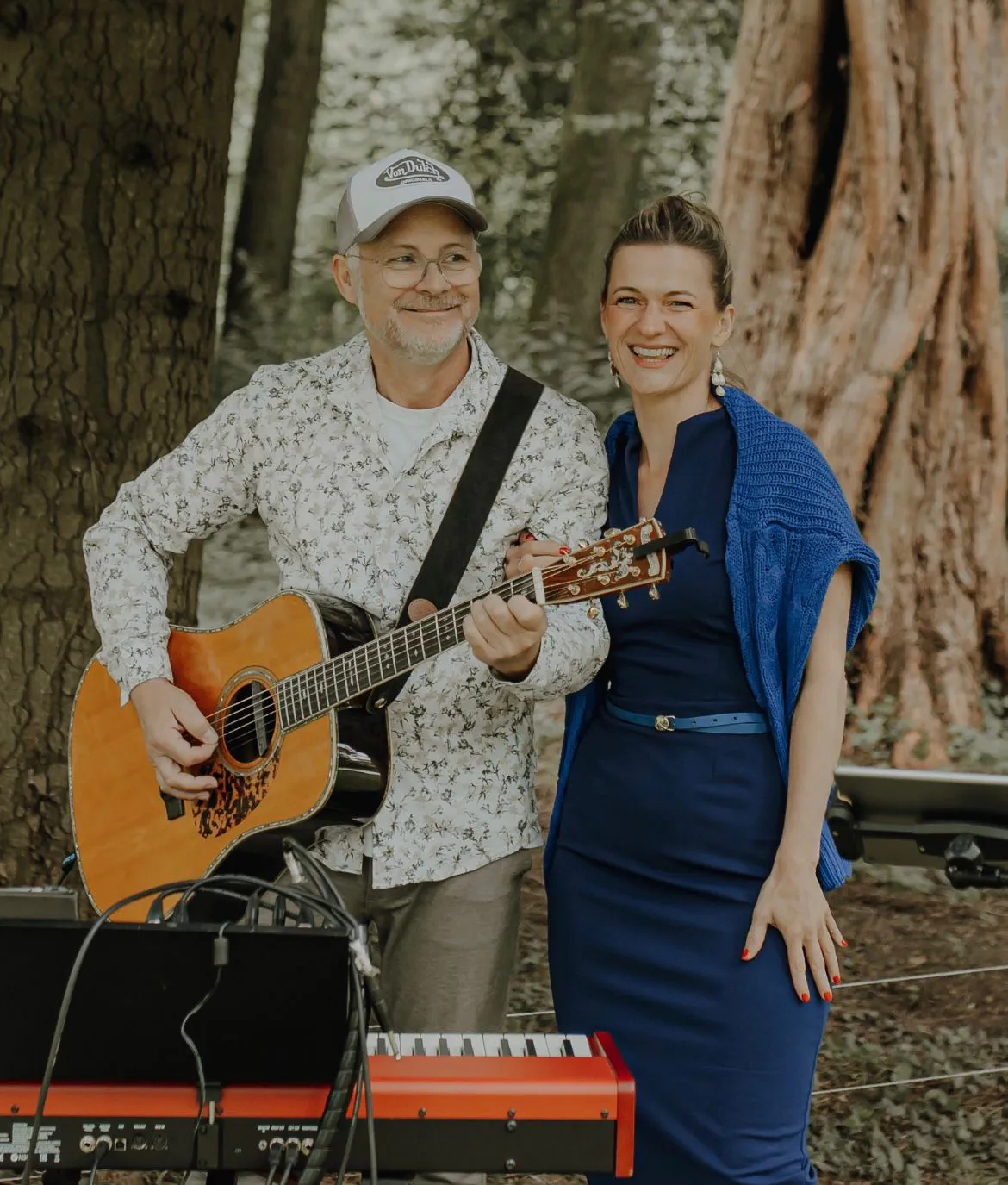 Dana und Stefan mit Gitarre und Klavier zwischen alten Bäumen